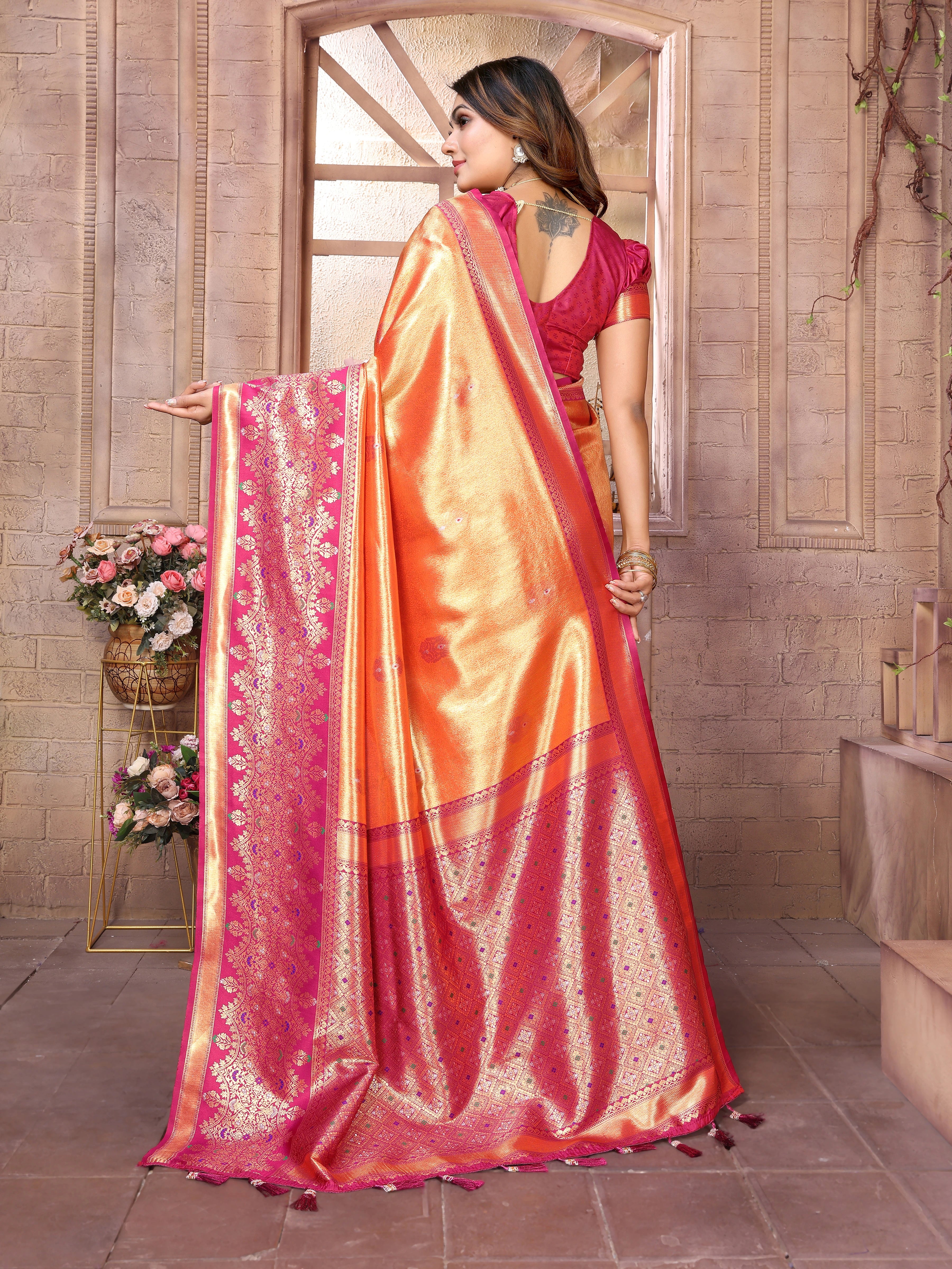 Woman wearing a vibrant orange and pink saree with a floral background
