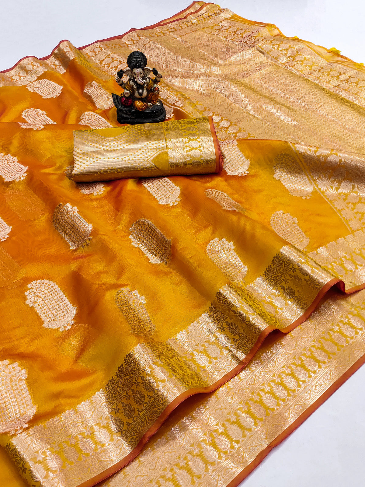 Orange and gold saree with a decorative item on a white background