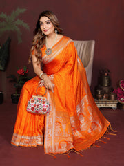 Woman in an orange saree with a decorative bag, sitting against a dark background.