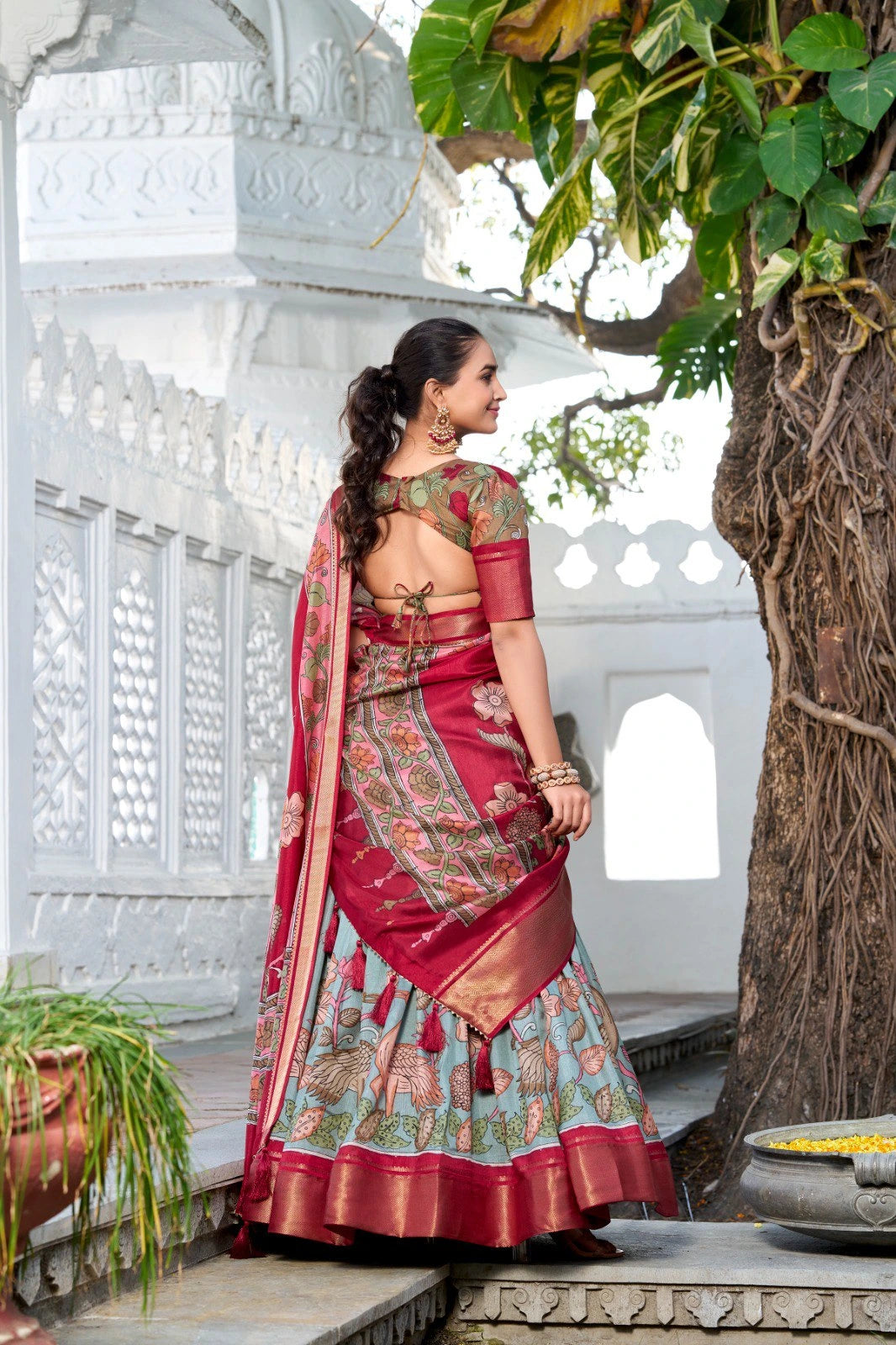 Elegant woman wearing a floral print lehenga with embroidered blouse and contrasting dupatta in a heritage palace setting.
