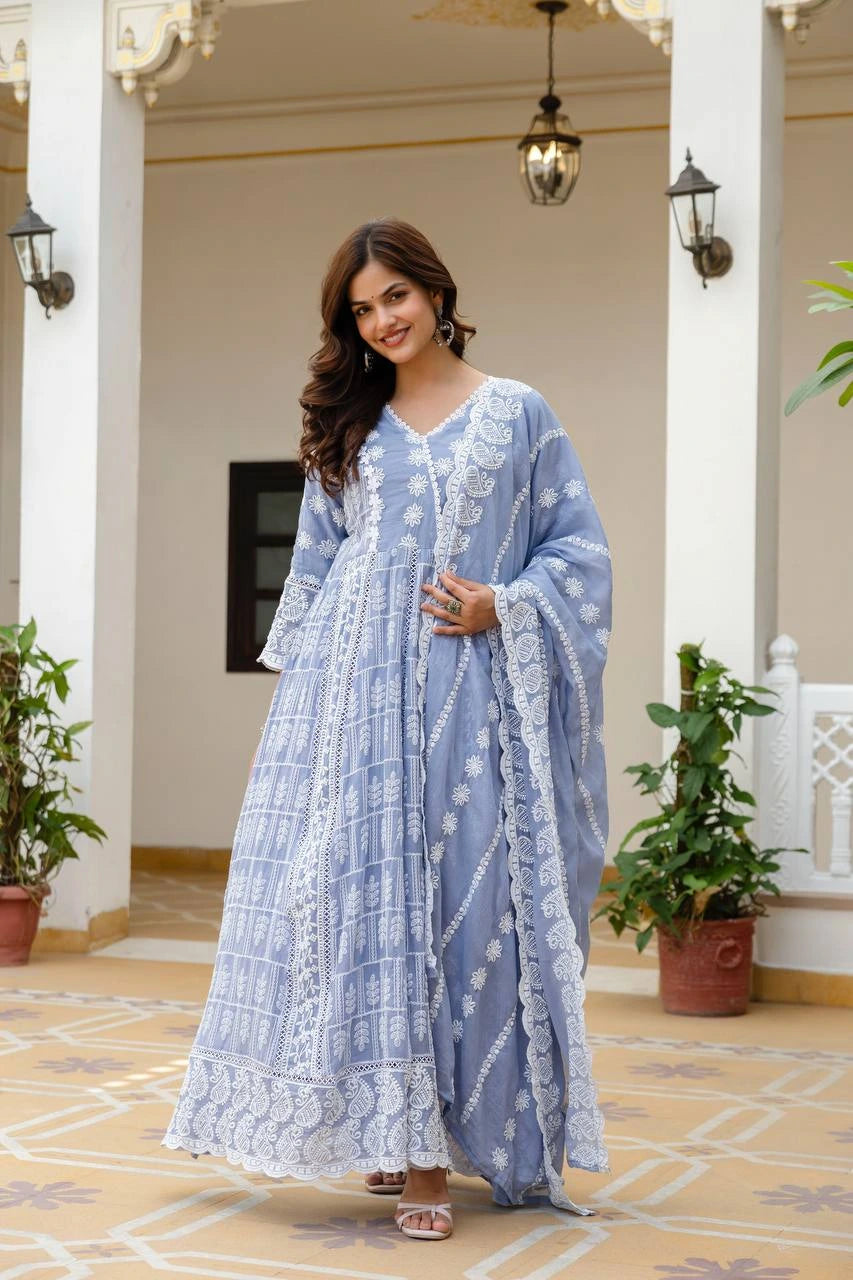 Woman in a light blue traditional outfit standing in an elegant indoor setting with plants and decorative lights.