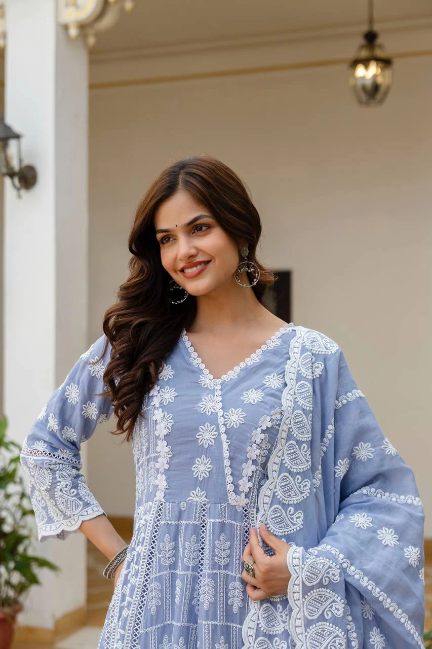 Woman wearing a light blue dress with white embroidery in an outdoor setting.