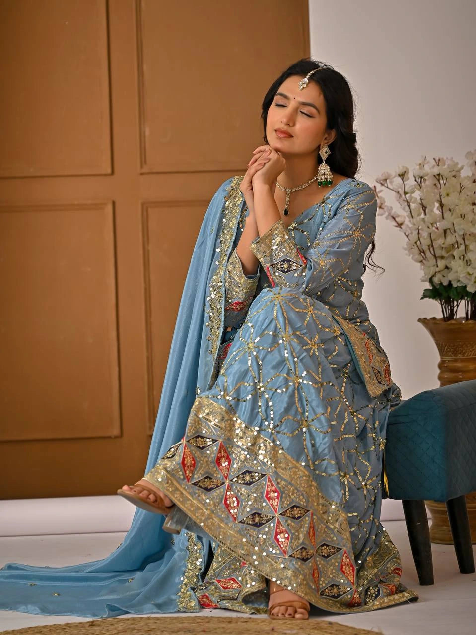 Woman in a traditional blue and gold embroidered outfit with a neutral background