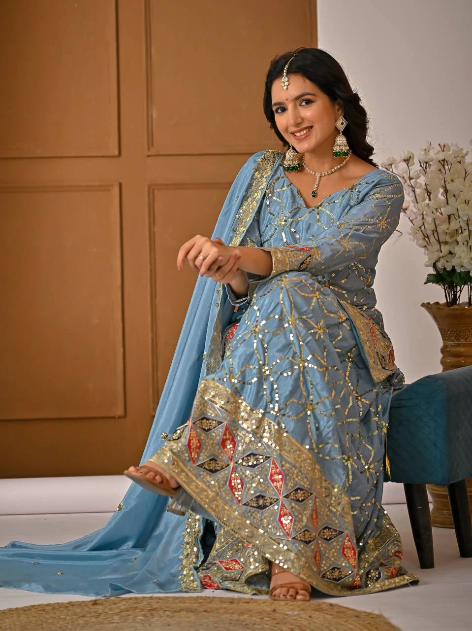 Woman in a blue and gold traditional outfit sitting on a couch.