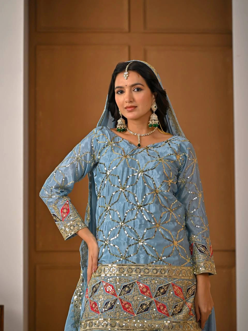Woman wearing a traditional embroidered outfit with jewelry against a neutral background