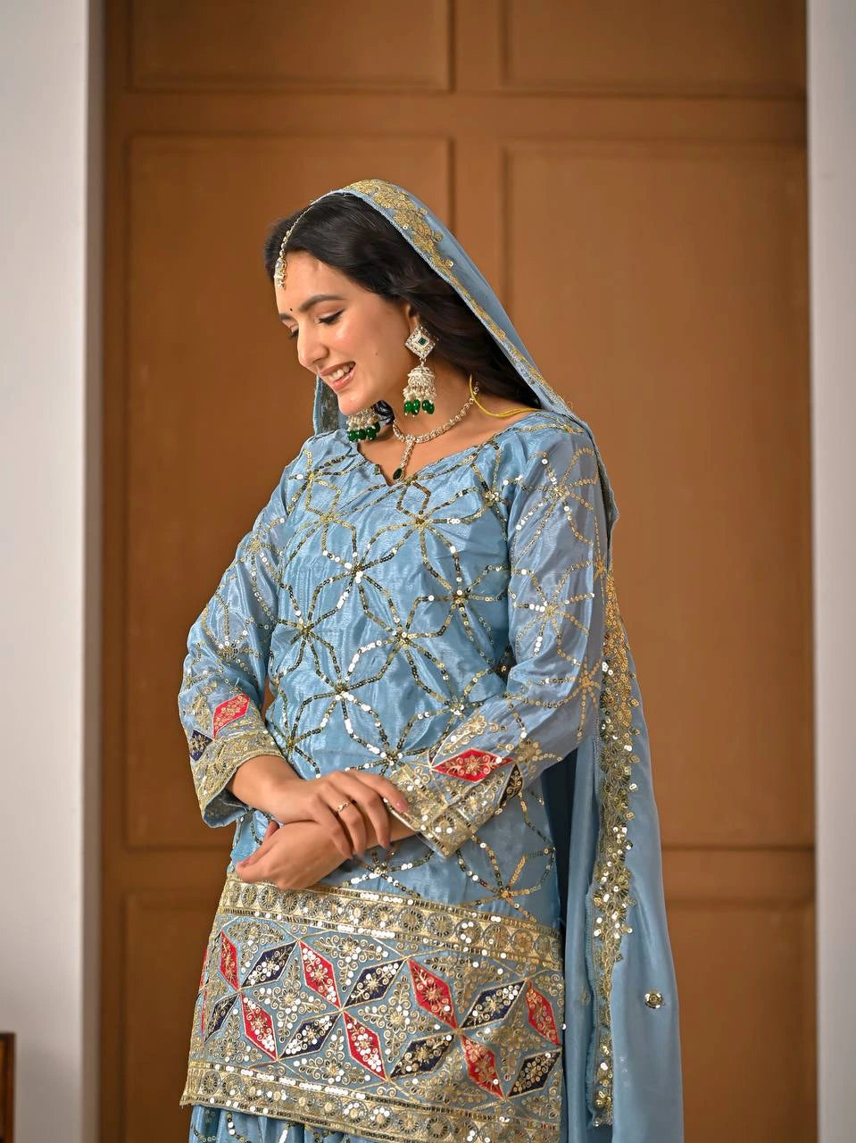 Woman in traditional blue embroidered outfit with gold details against a wooden door background
