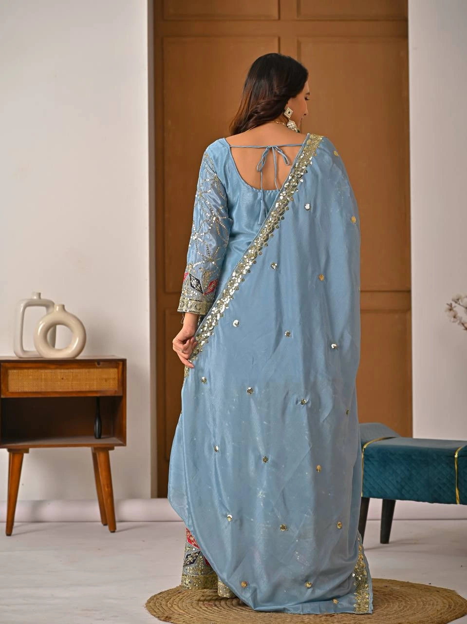 Woman wearing a light blue saree with gold embroidery in a room setting.