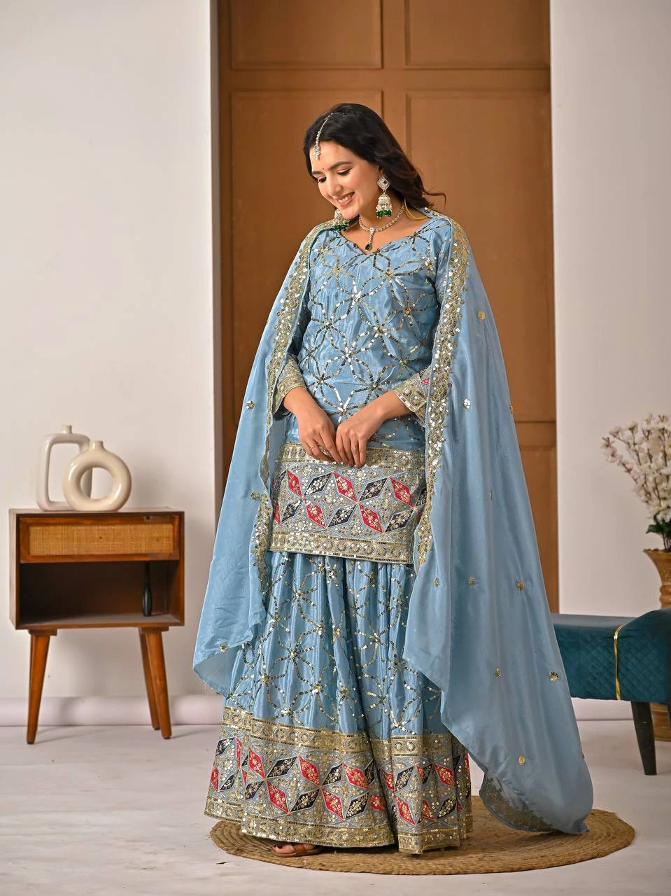 Woman in a traditional blue embroidered outfit with a matching dupatta in a room.