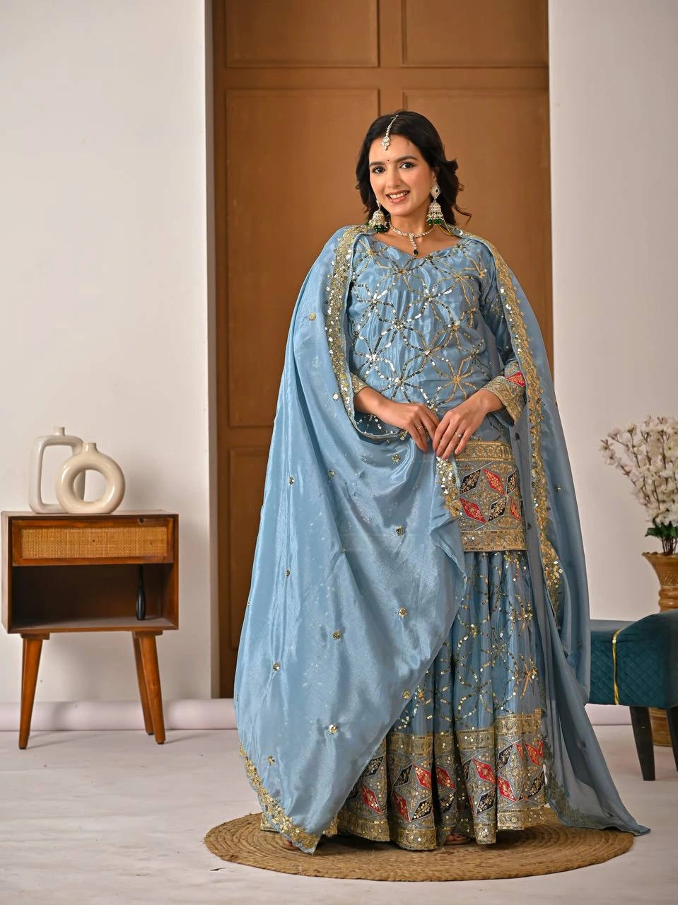 Woman in a traditional light blue embroidered outfit standing indoors.