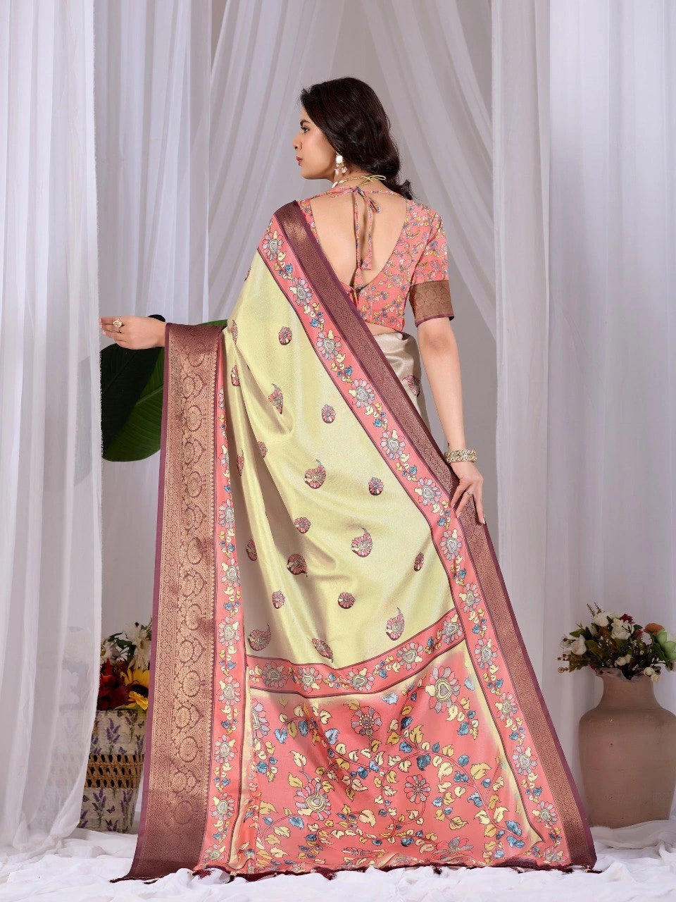 Woman wearing a light green saree with a pink blouse, standing against a white curtain background.