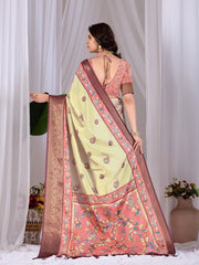 Woman wearing a light green saree with a pink blouse, standing against a white curtain background.