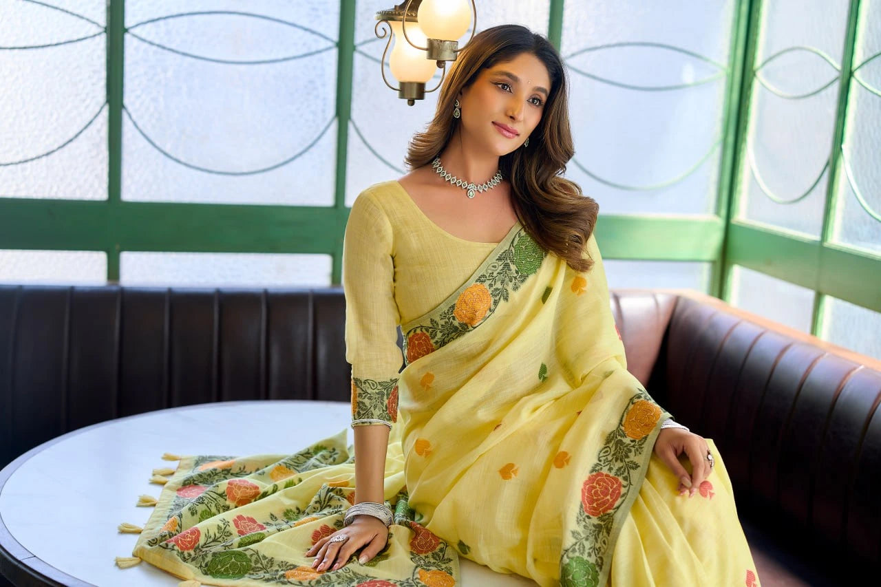 Woman in a yellow saree with floral patterns sitting on a couch.