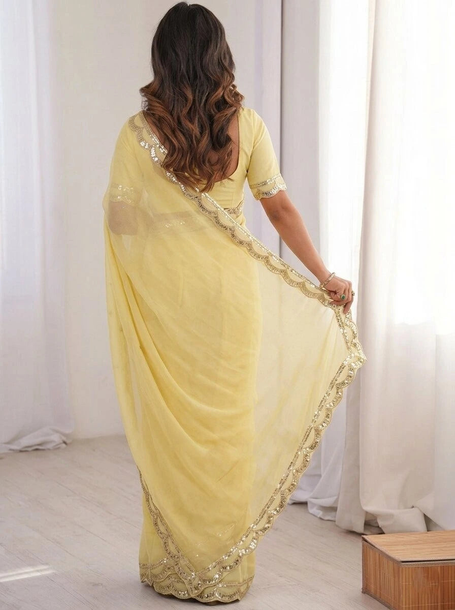 Woman wearing a yellow saree with gold border in a room with white curtains.