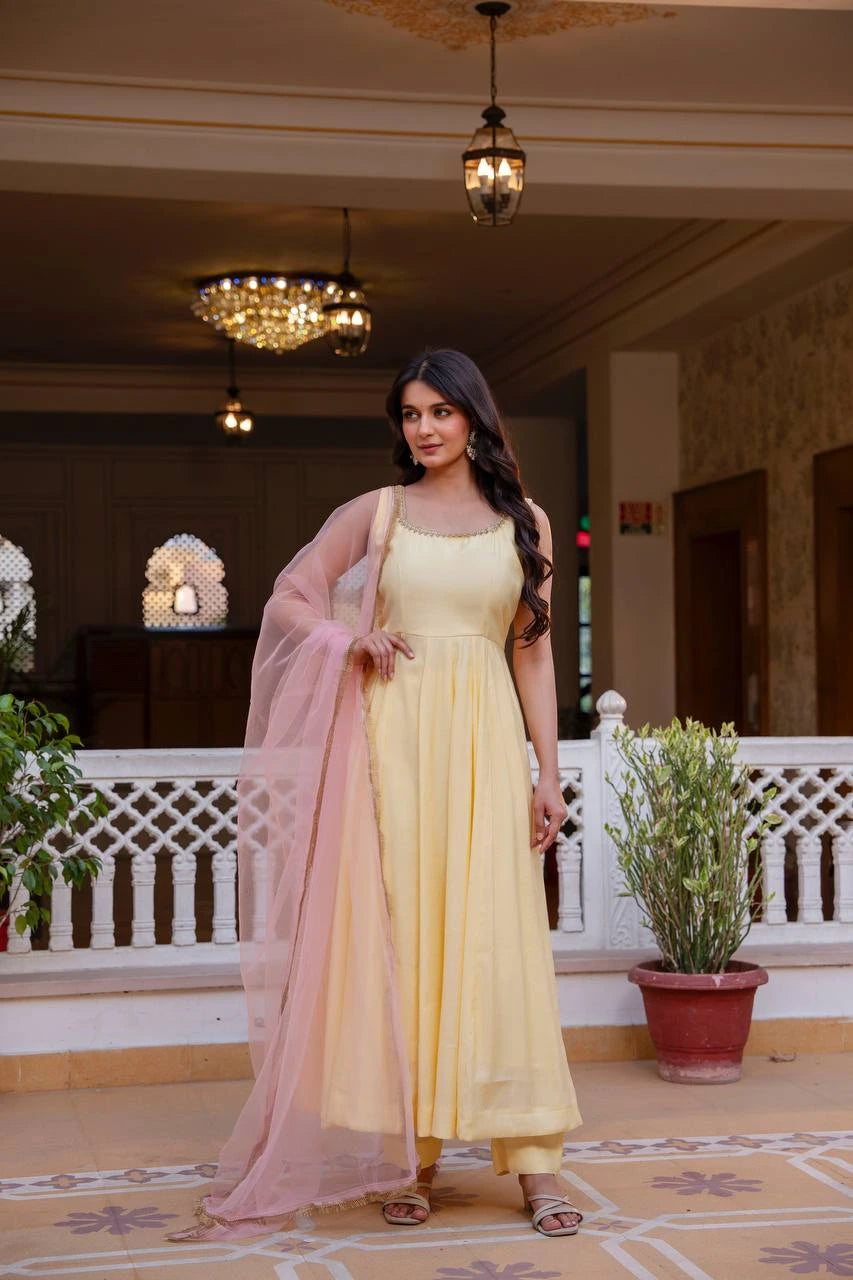 Woman in a yellow dress with a pink dupatta standing in an elegant indoor setting.