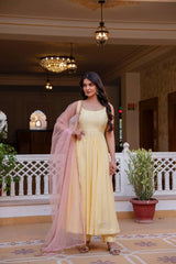 Woman in a yellow dress with a pink dupatta standing in an elegant indoor setting.