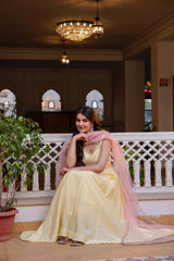 Woman in a yellow and pink traditional outfit sitting on a balcony with decorative lights and plants.
