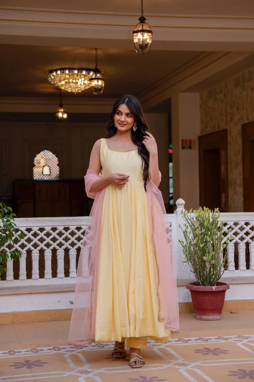 Woman in a yellow dress with a pink dupatta standing in an indoor setting with decorative lights and plants.