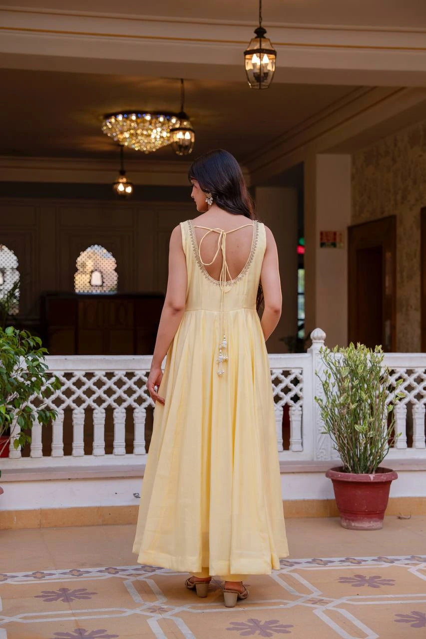 Woman in a yellow dress standing in a decorated indoor setting with chandeliers and plants.