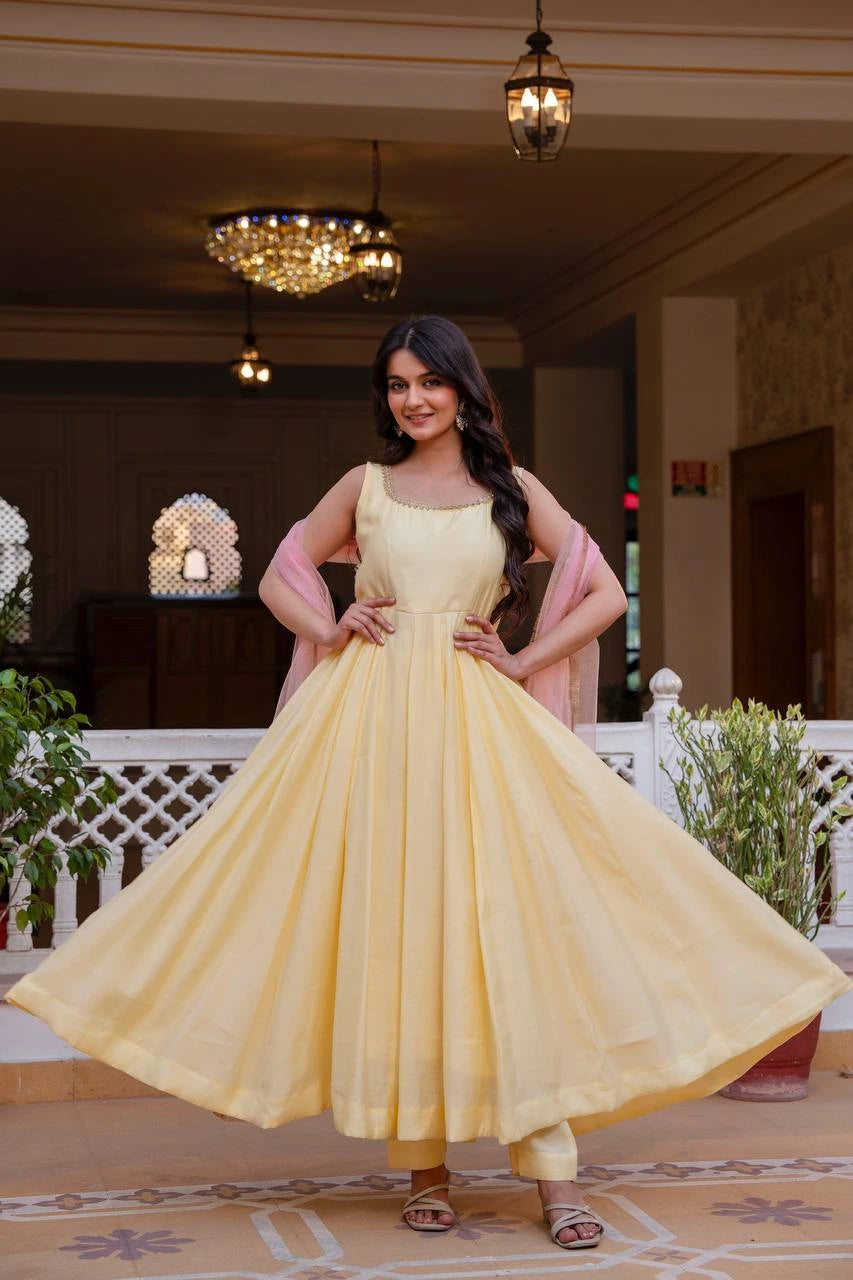 Woman in a yellow dress with pink dupatta standing in an indoor setting.