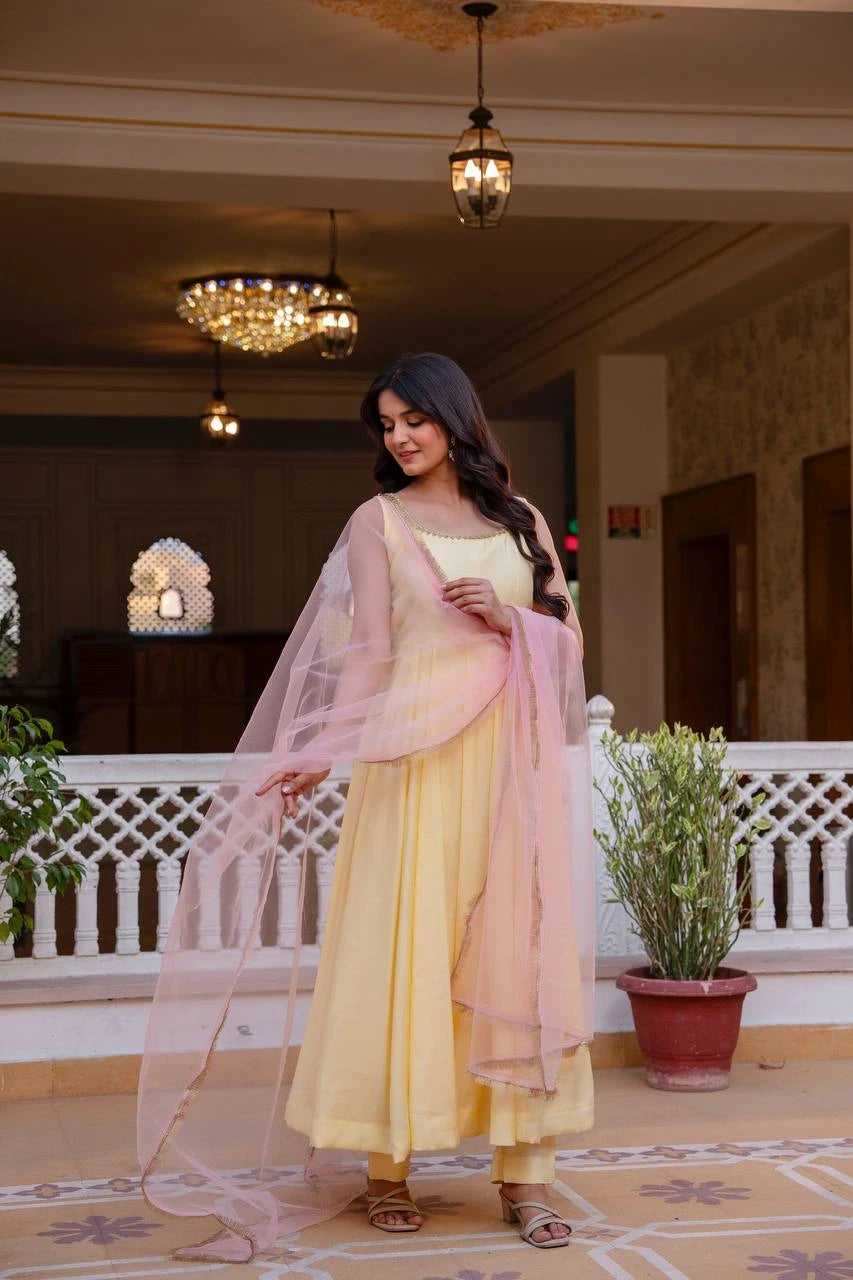 Woman in a yellow and pink traditional outfit standing in an elegant indoor setting.
