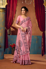 Woman in a pink saree with a decorative border standing in front of red curtains.