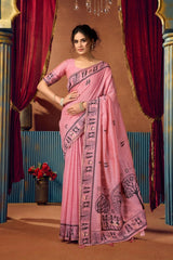 Woman wearing a pink saree with black patterns in a decorated indoor setting.