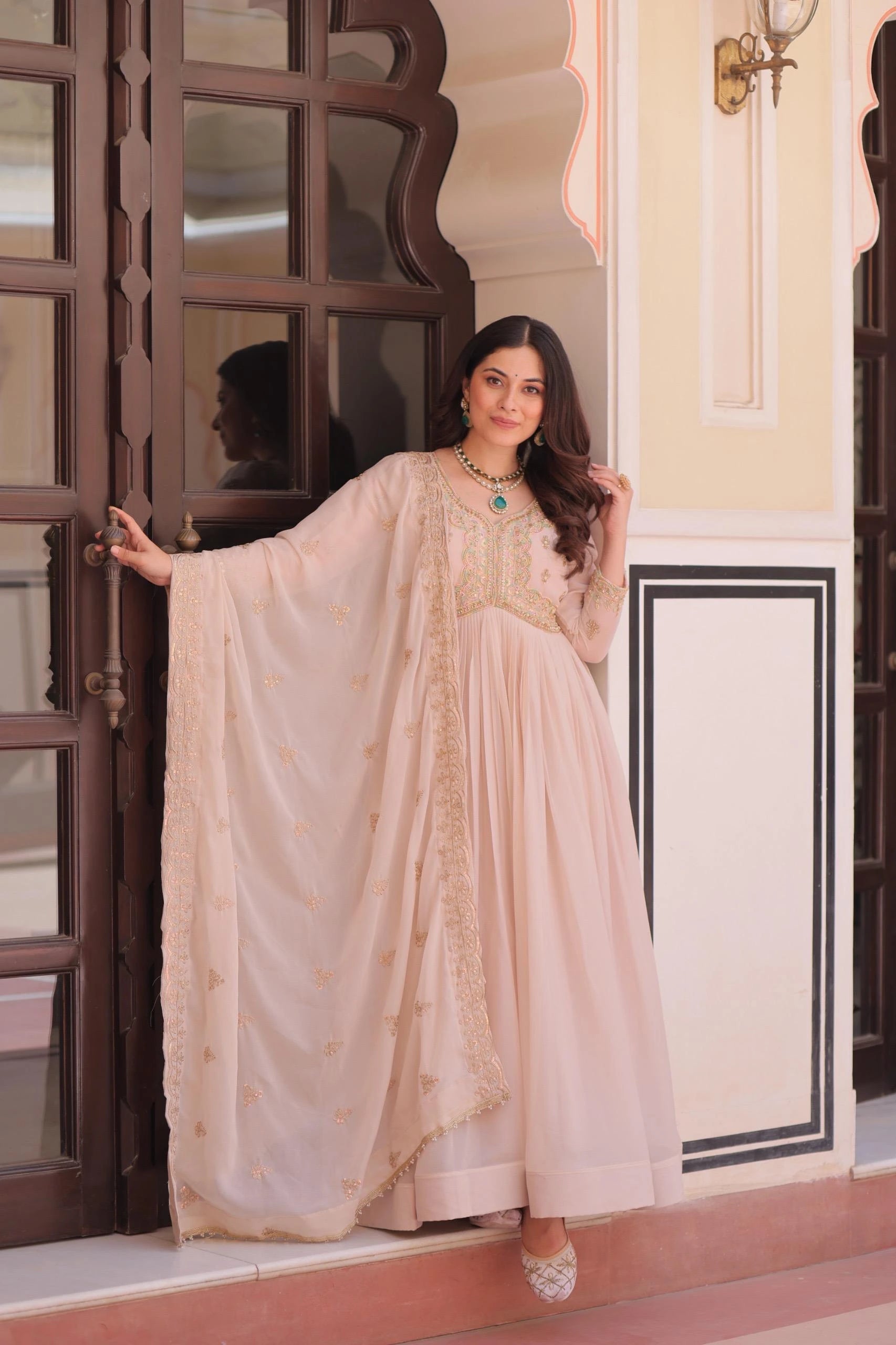 Woman in a beige saree standing in front of a decorative door.