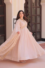 Woman in a flowing beige dress standing indoors with decorative elements in the background