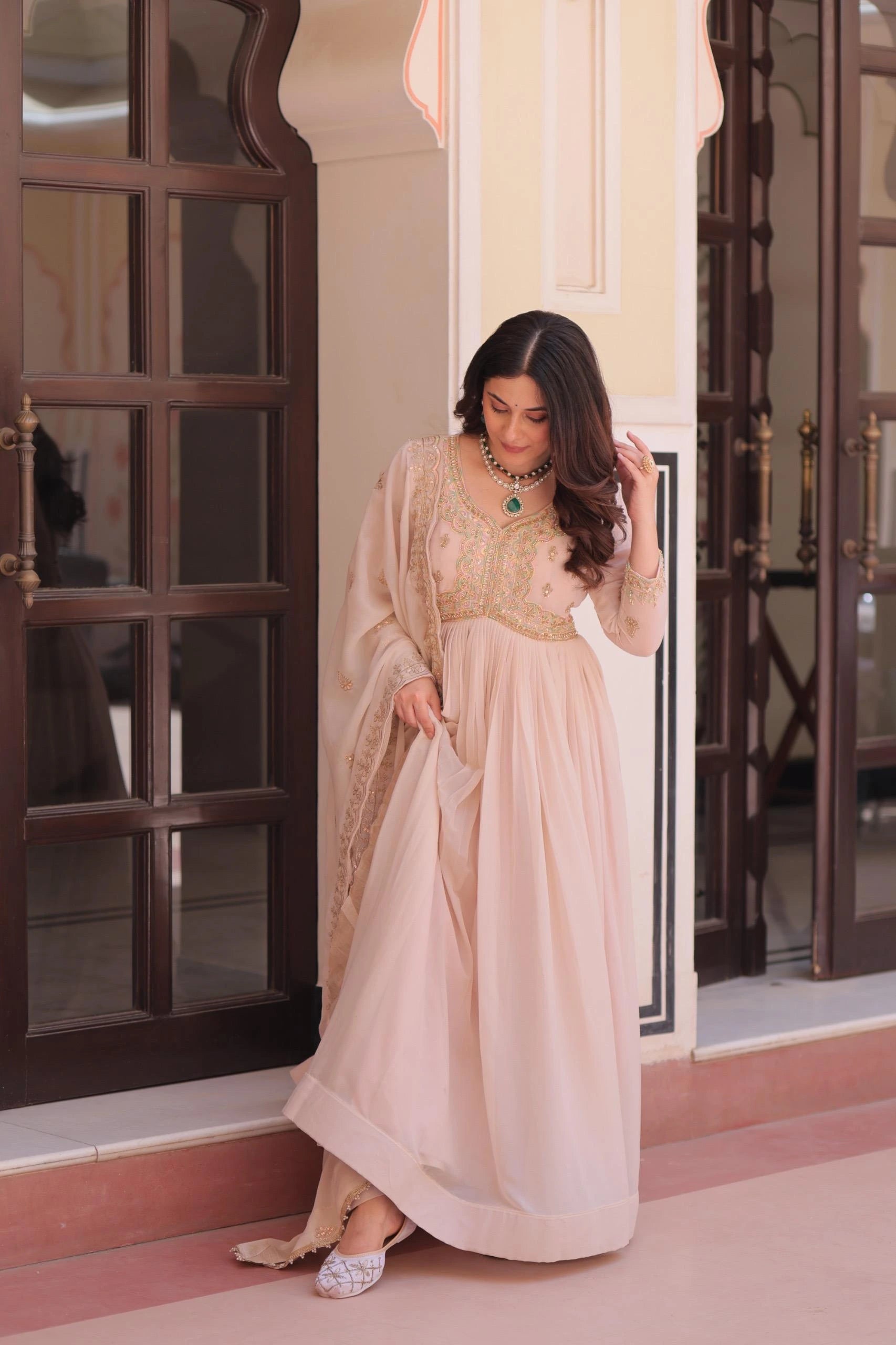 Woman in a beige traditional outfit standing in a doorway.