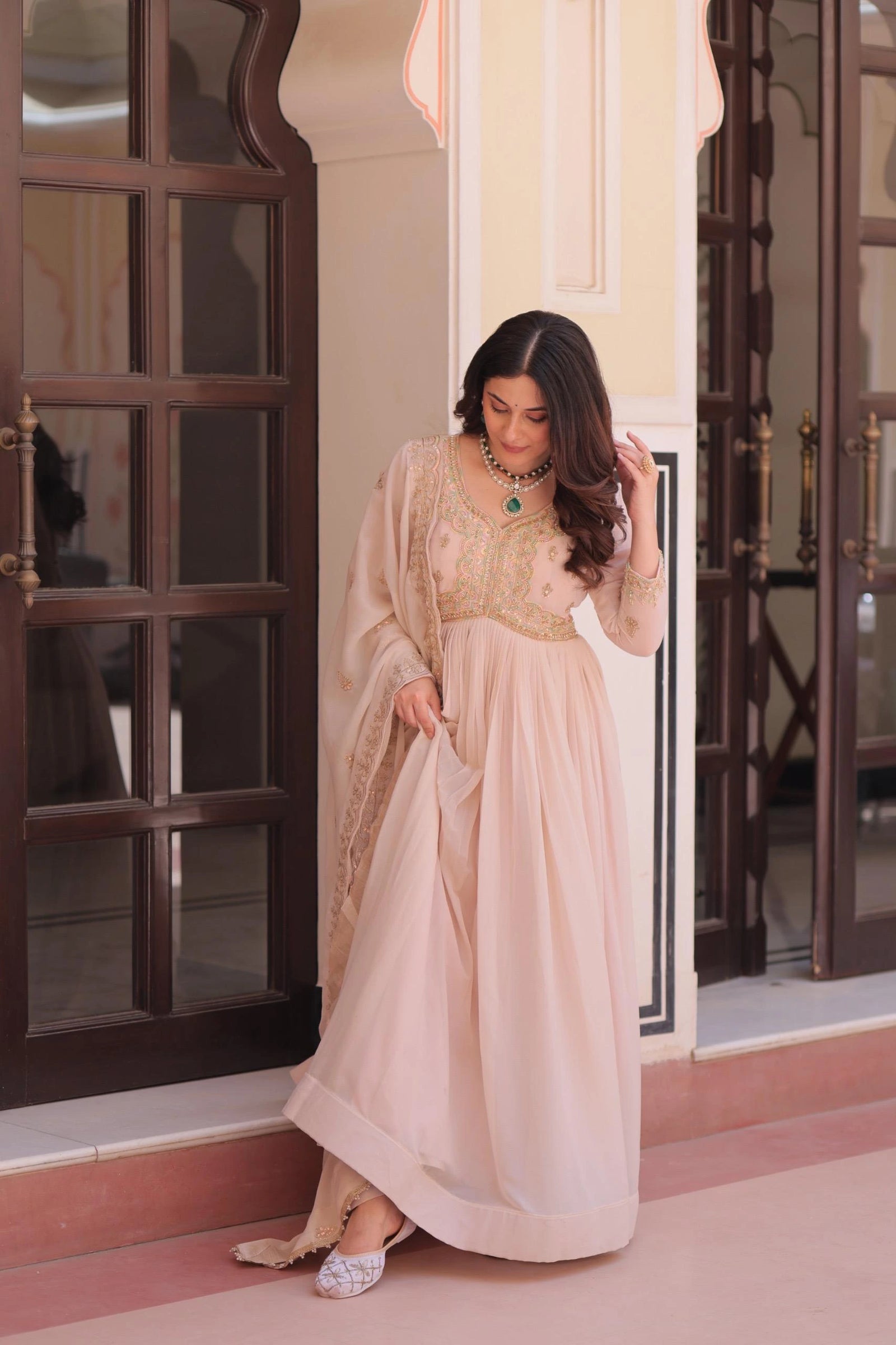 Woman in a beige traditional outfit standing in a doorway.