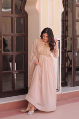 Woman in a beige traditional outfit standing in a doorway.