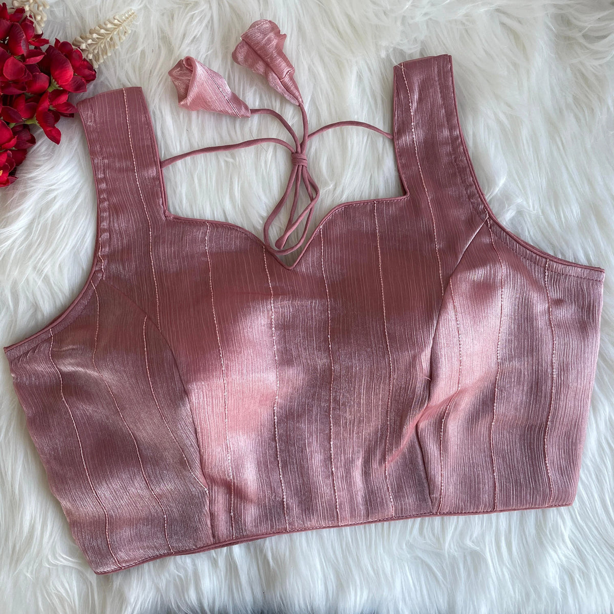 Pink crop top with thin straps on a white fur surface with red flowers.