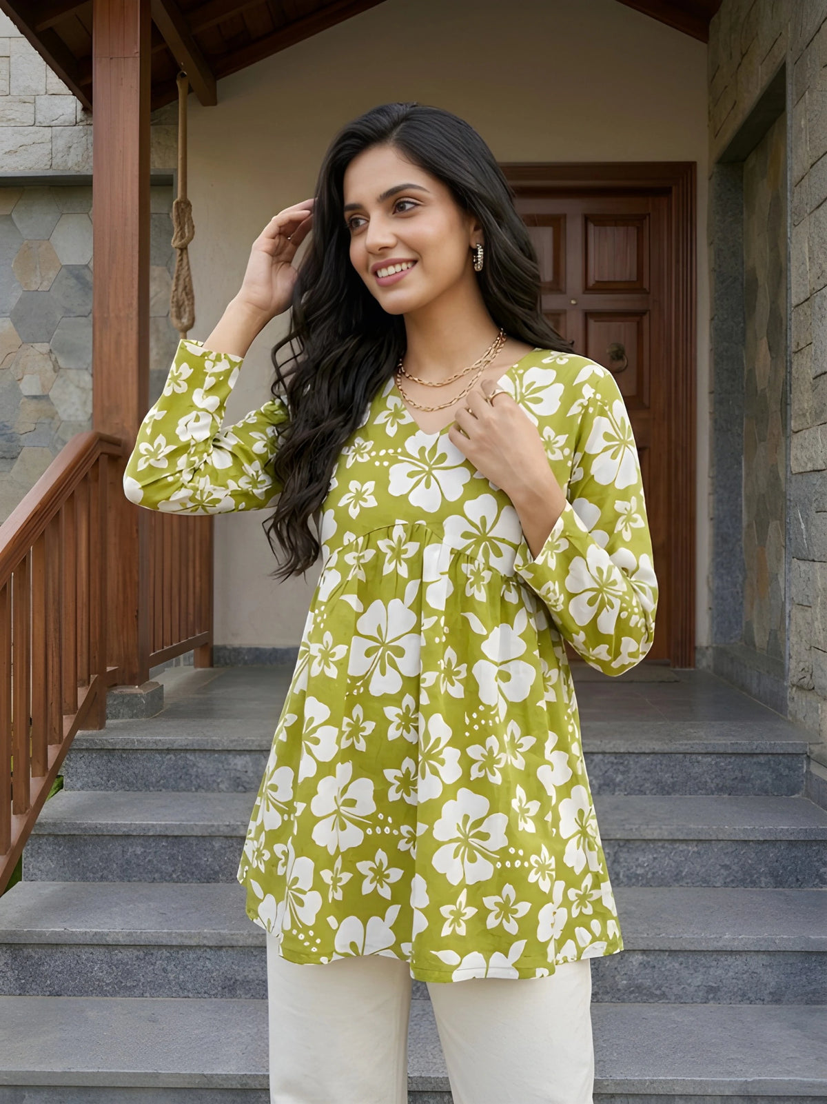 Woman wearing a green floral top standing on steps outside a building.