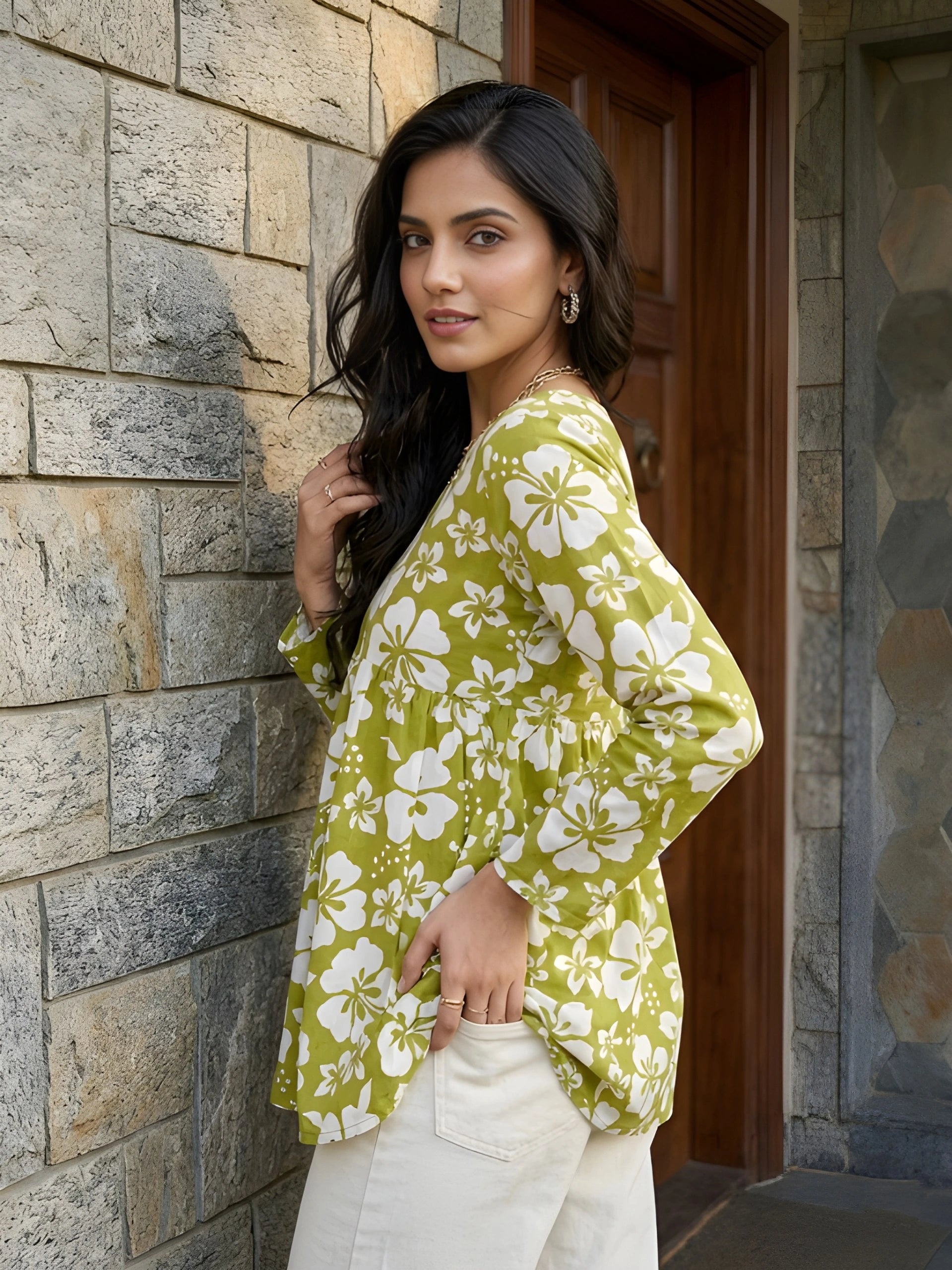 Woman wearing a green floral kimono standing against a stone wall.