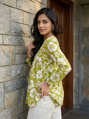Woman wearing a green floral kimono standing against a stone wall.