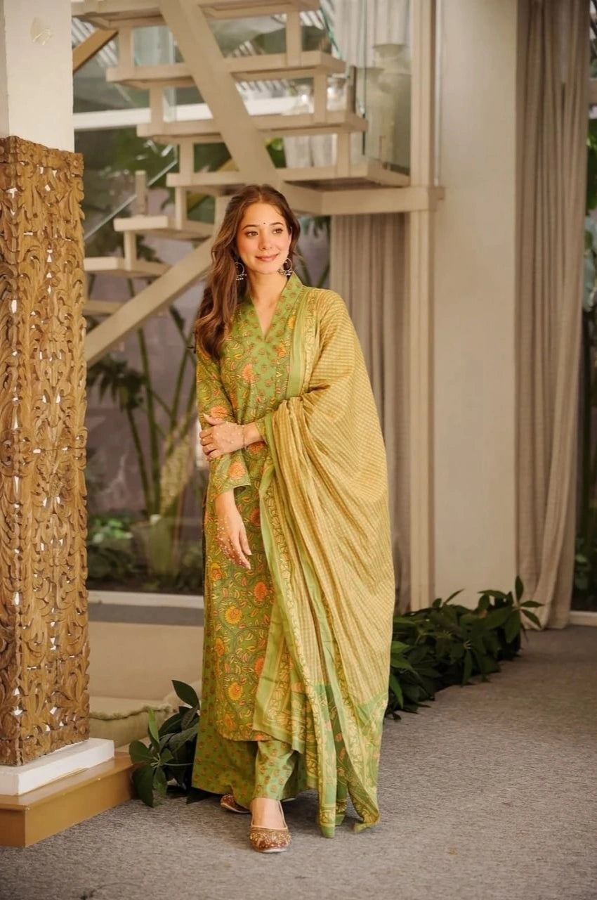 Woman in a green traditional outfit standing indoors with decorative elements.