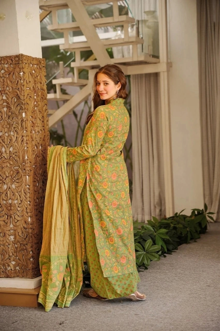 Woman in a green traditional outfit standing indoors with decorative elements.