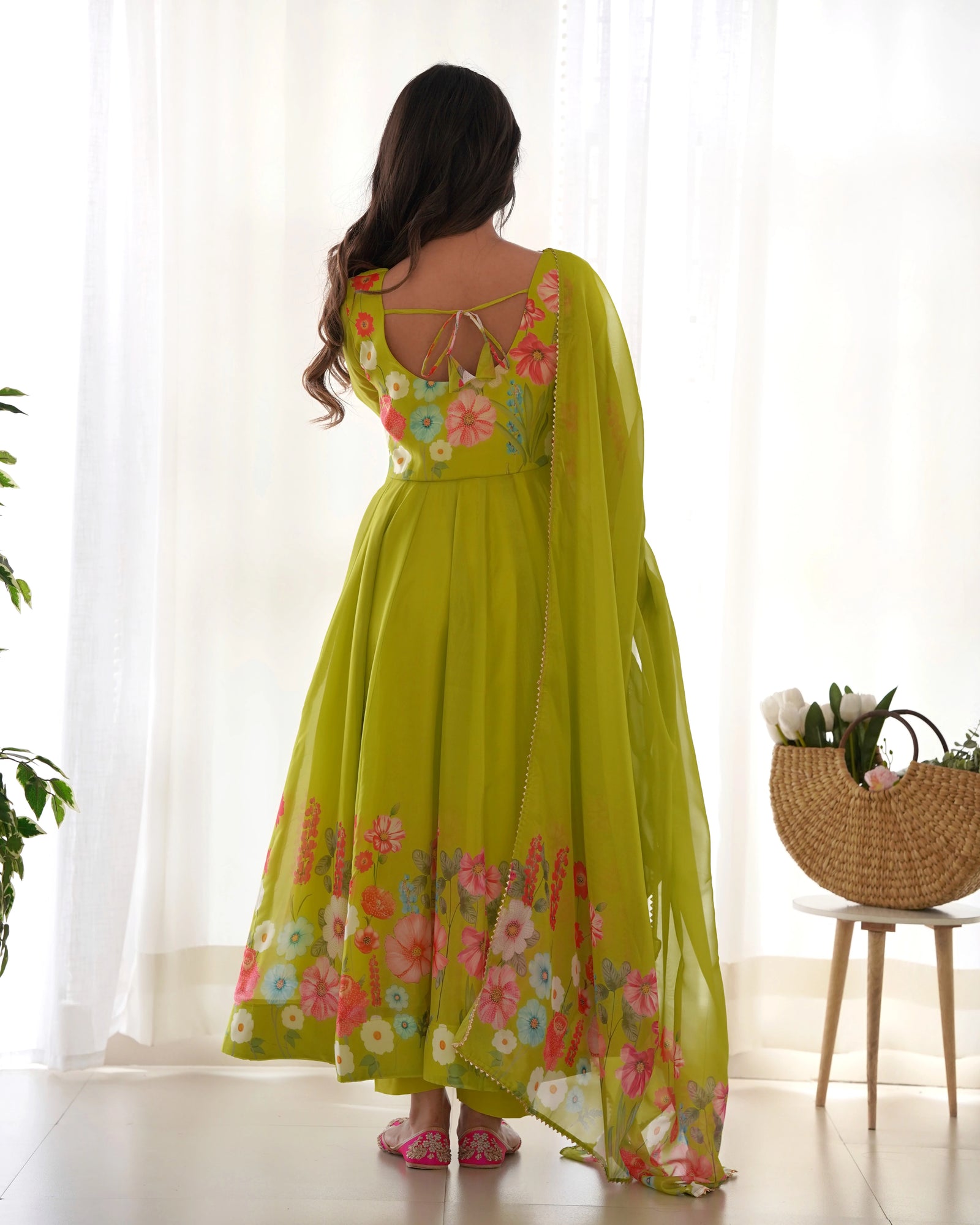 Woman wearing a green floral dress standing in a bright room with sheer curtains.