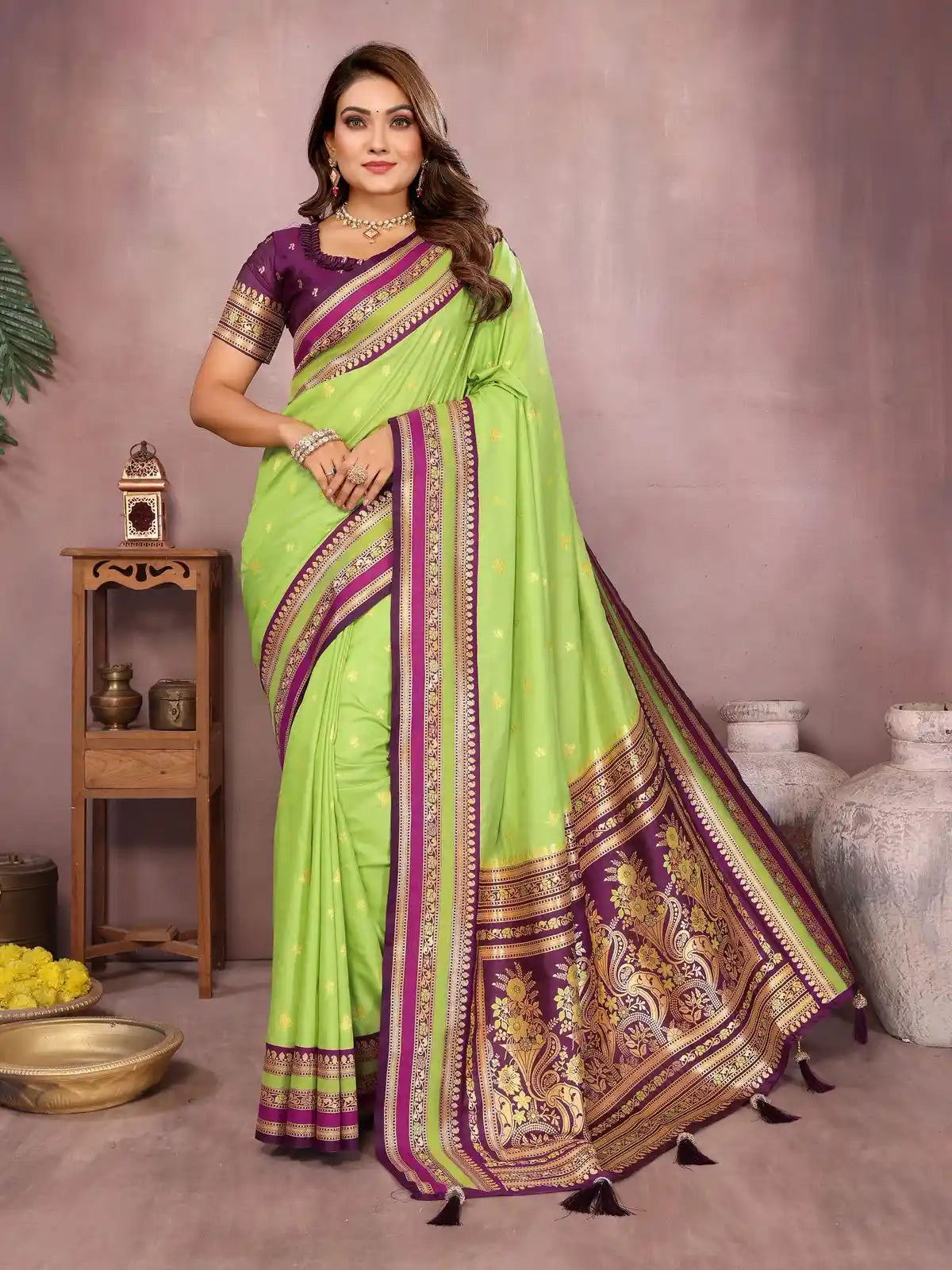 Woman wearing a green and purple saree with a decorative border in a room setting.