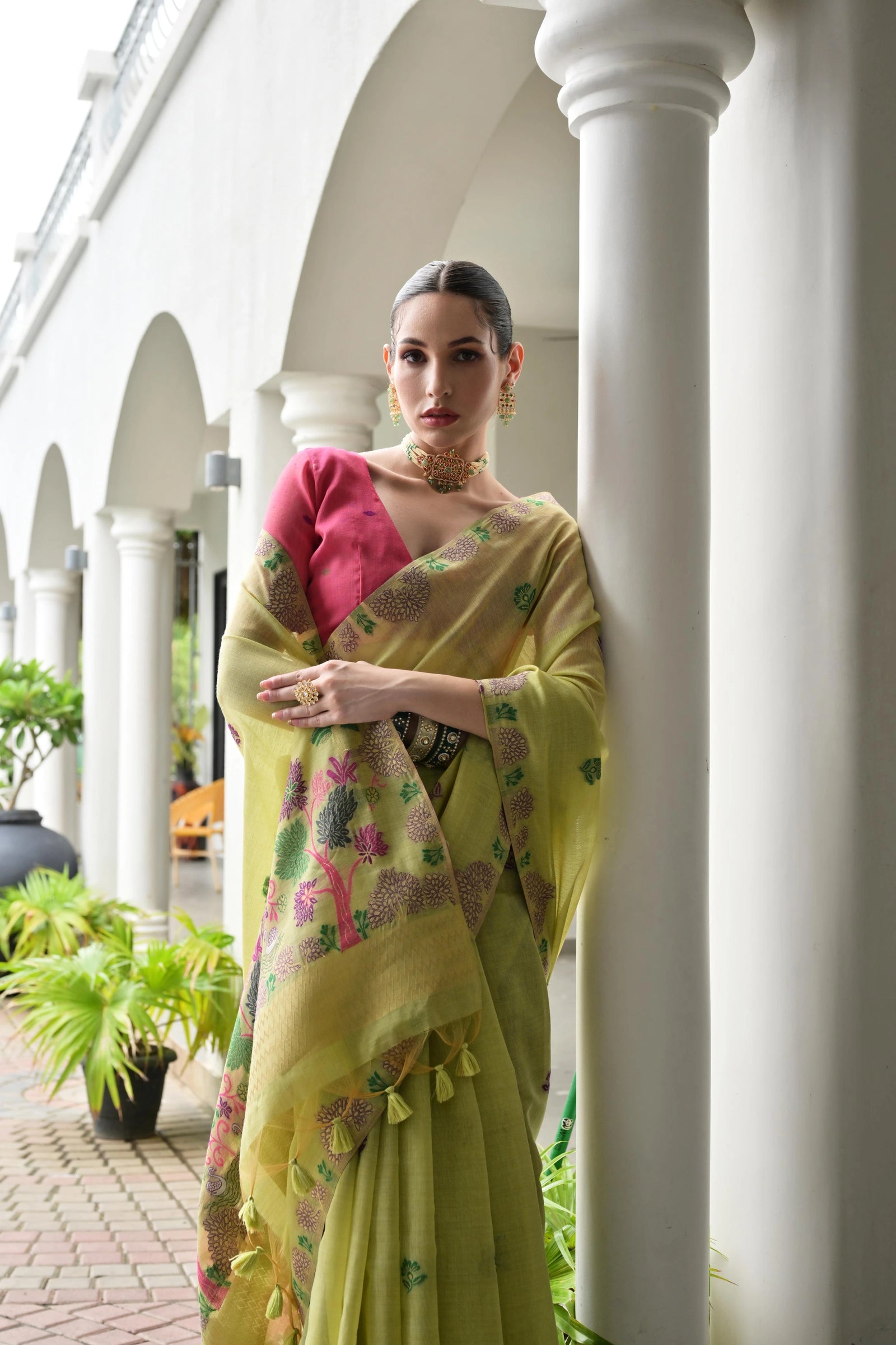Woman in a yellow saree with a pink blouse standing in front of white columns.