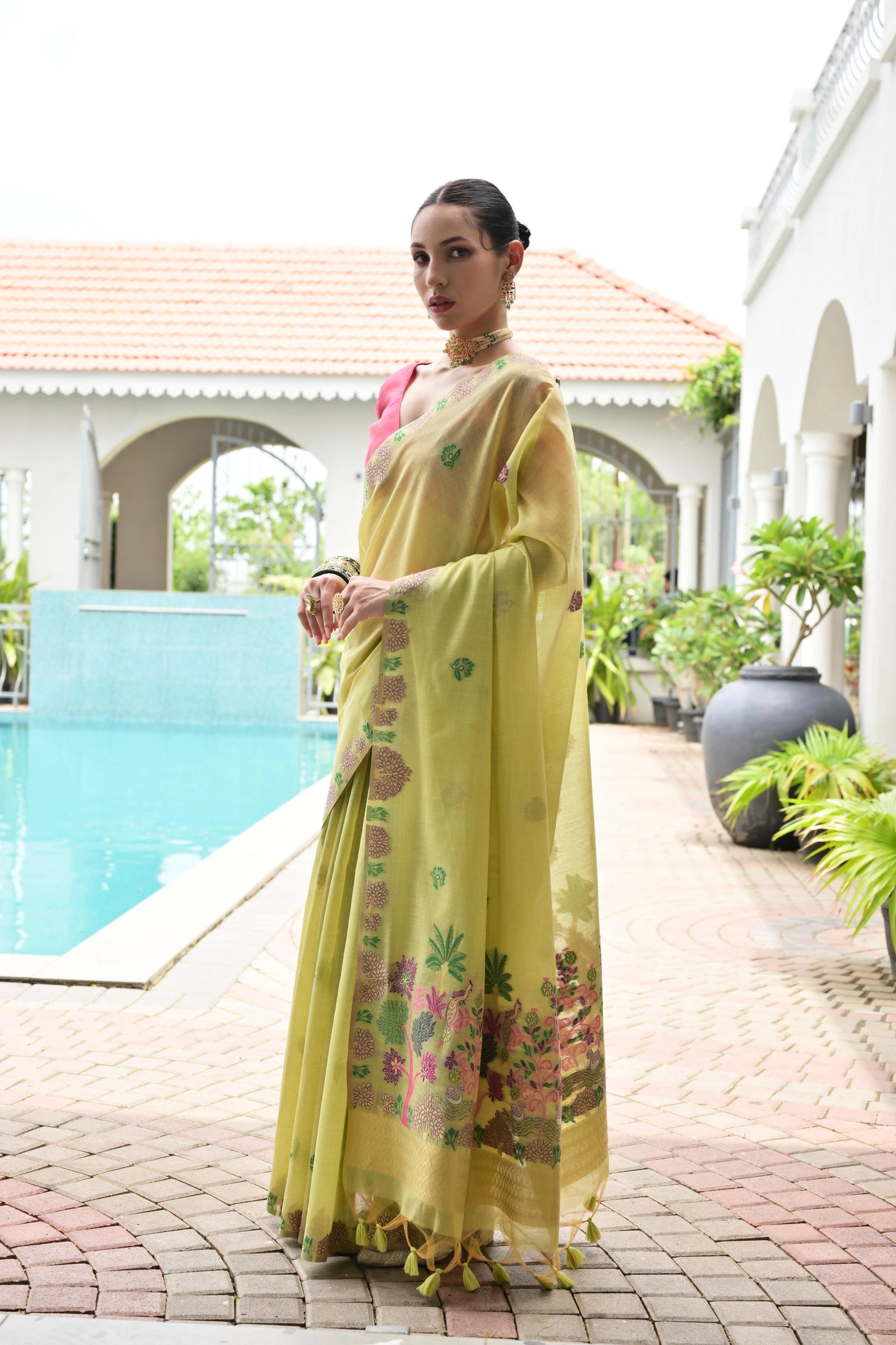 Woman in a yellow saree with floral patterns standing by a poolside.