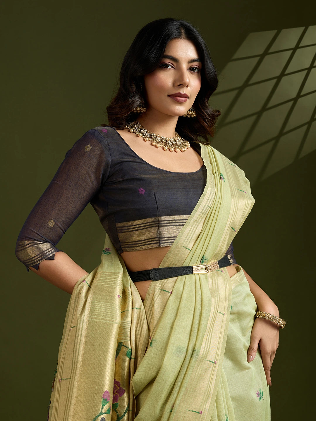 Woman wearing a traditional outfit with a green saree and black blouse against a dark background