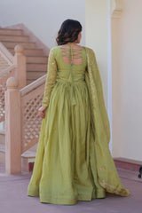 Woman in a green traditional outfit standing in a decorative interior setting.