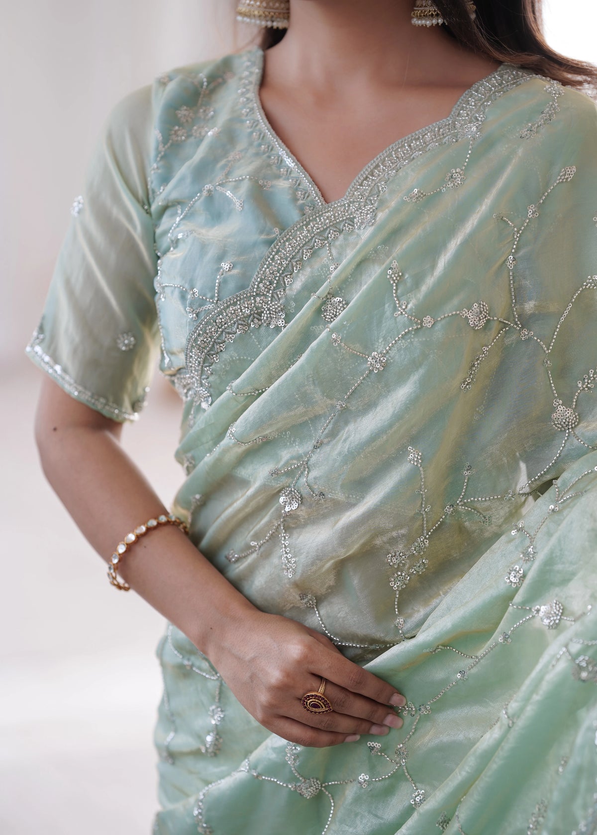 Light green saree with intricate patterns and embellishments on a plain background