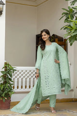 Woman in a light green traditional outfit standing in an indoor setting with plants.