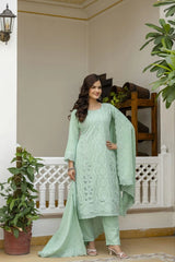 Woman in a light green traditional outfit standing in a decorated indoor setting with plants.