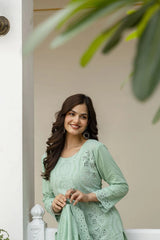Woman in a light green traditional outfit standing indoors with a neutral background