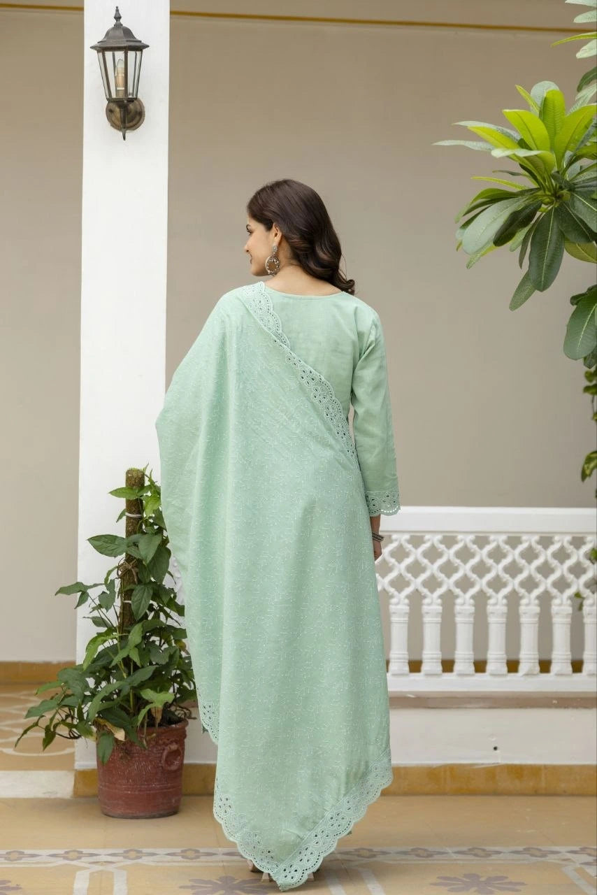 Woman in a light green dress standing in a decorative indoor setting with plants and a white railing.