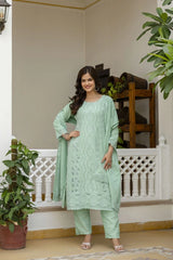Woman in a light green traditional outfit standing in a decorated indoor setting with plants.