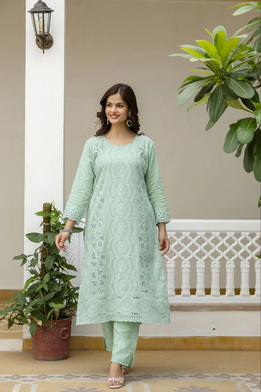Woman in a light green traditional outfit standing in a decorative indoor setting with plants.